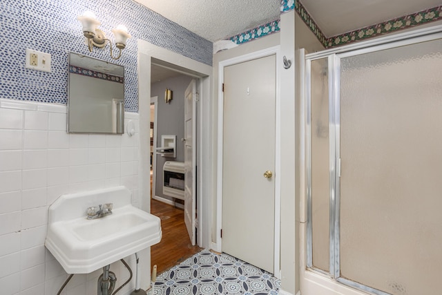 bathroom featuring a shower with shower door, tile walls, heating unit, and a textured ceiling