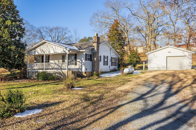 view of front of house featuring a front yard, covered porch, a garage, and an outbuilding