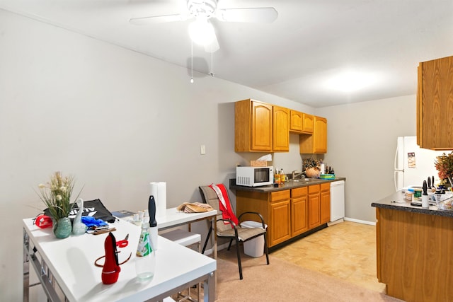 kitchen featuring dark countertops, white appliances, baseboards, ceiling fan, and a sink