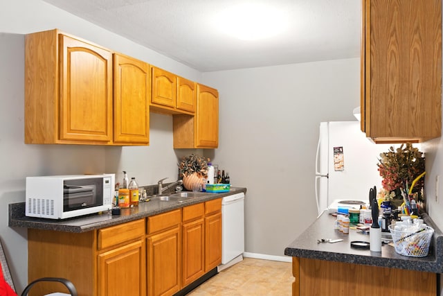 kitchen featuring a sink, dark countertops, light tile patterned flooring, and white appliances