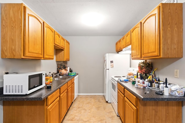 kitchen featuring dark countertops, a sink, white appliances, baseboards, and under cabinet range hood