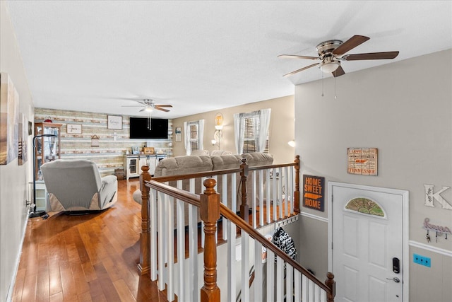 corridor featuring an upstairs landing, wooden walls, light wood-style flooring, and an accent wall