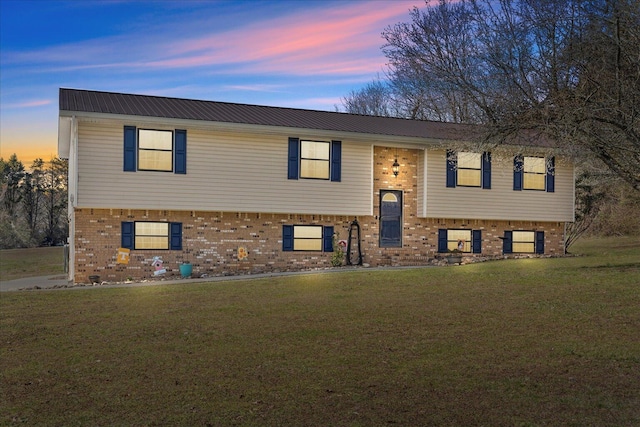 raised ranch with brick siding, a lawn, and metal roof