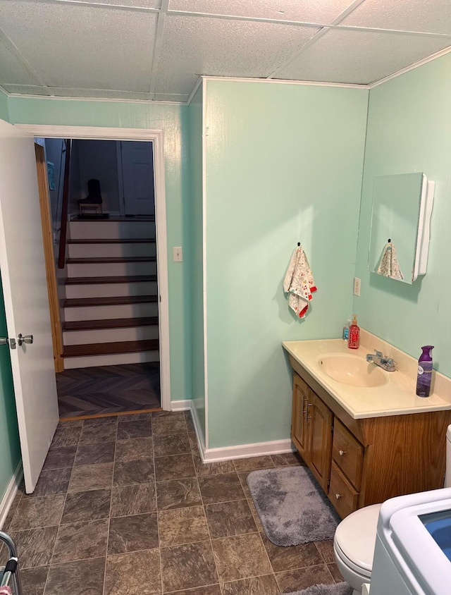 bathroom featuring a drop ceiling, baseboards, toilet, and vanity