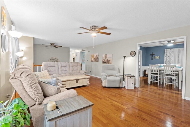 living area with baseboards, light wood-type flooring, and a ceiling fan