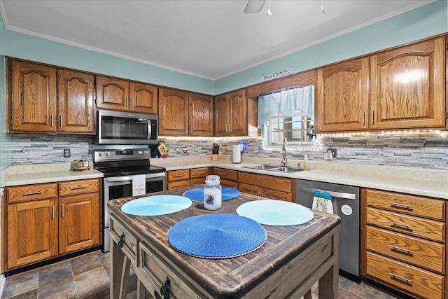 kitchen featuring brown cabinetry, a sink, appliances with stainless steel finishes, stone finish flooring, and backsplash