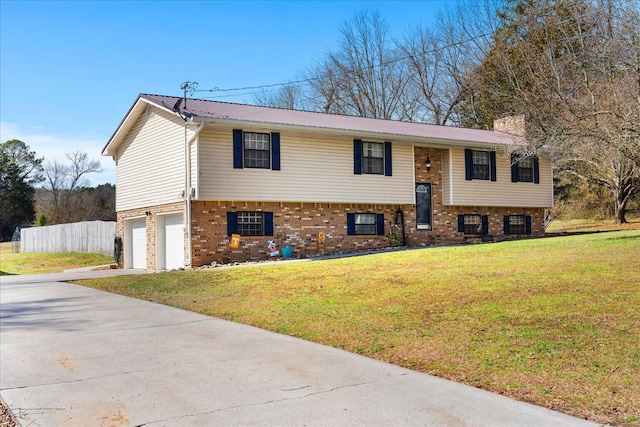 split foyer home featuring a front yard, driveway, a chimney, brick siding, and metal roof