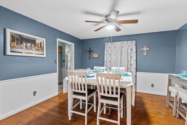 dining space featuring a ceiling fan, wood finished floors, and wainscoting