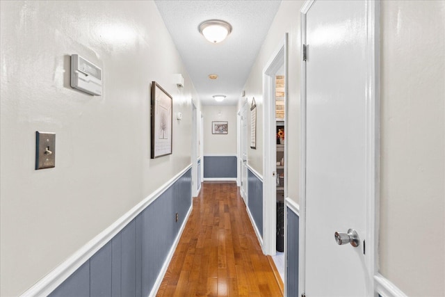 corridor with a textured ceiling, wood finished floors, and wainscoting