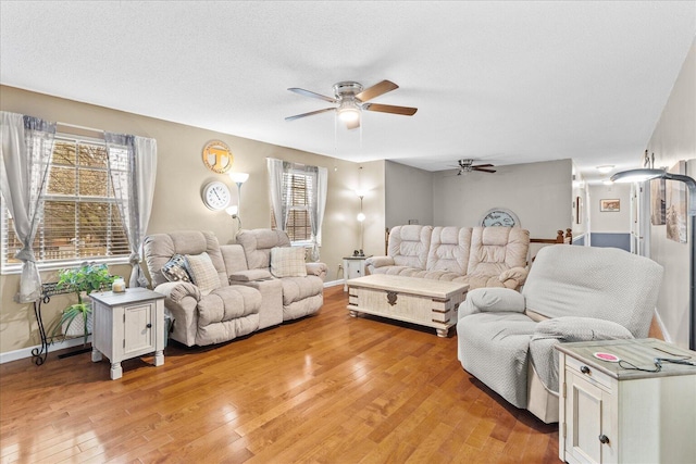 living room with light wood-type flooring, plenty of natural light, baseboards, and a ceiling fan