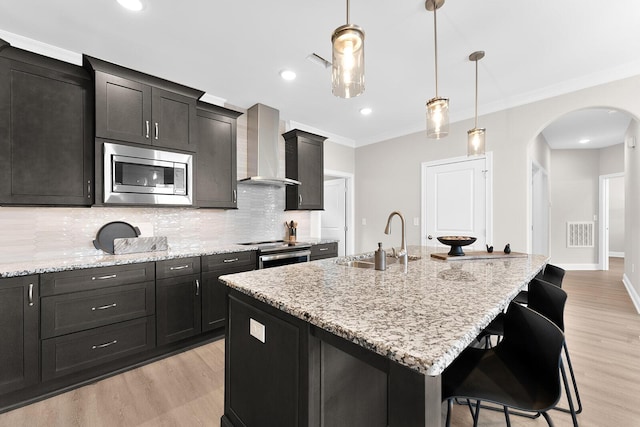 kitchen featuring visible vents, arched walkways, a sink, stainless steel appliances, and wall chimney range hood