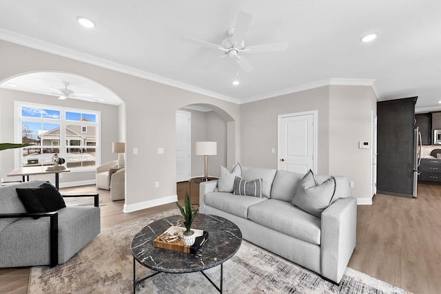 living room featuring arched walkways, light wood finished floors, ceiling fan, and ornamental molding
