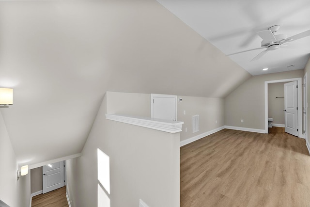 additional living space featuring visible vents, a ceiling fan, light wood-style floors, baseboards, and vaulted ceiling