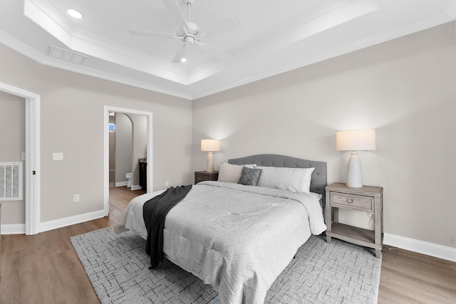 bedroom with visible vents, a raised ceiling, baseboards, and wood finished floors