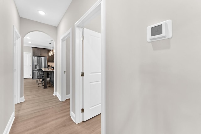 corridor featuring recessed lighting, baseboards, arched walkways, and light wood finished floors