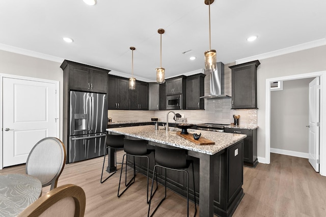 kitchen with appliances with stainless steel finishes, wall chimney exhaust hood, crown molding, light wood finished floors, and light stone countertops