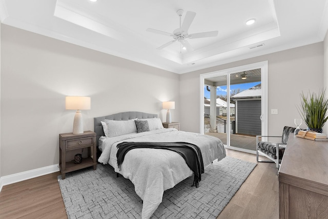 bedroom featuring access to exterior, visible vents, baseboards, light wood-type flooring, and a tray ceiling