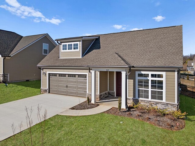 view of front of house with driveway, roof with shingles, an attached garage, a front lawn, and stone siding