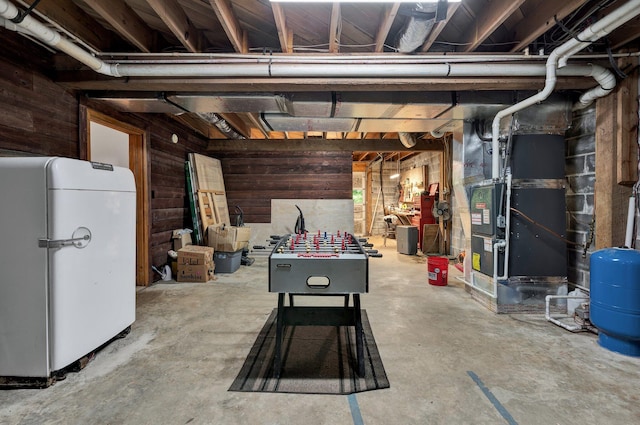 basement featuring heating unit, wood walls, and white refrigerator