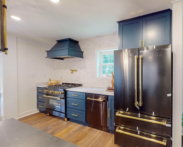 kitchen featuring tasteful backsplash, wood-type flooring, premium appliances, blue cabinetry, and custom range hood