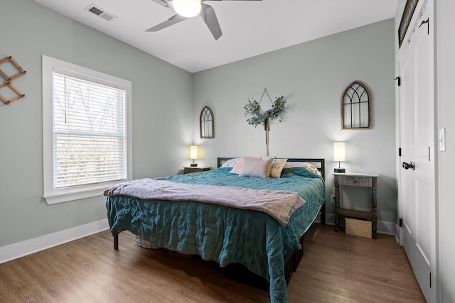 bedroom with a ceiling fan, wood finished floors, visible vents, and baseboards