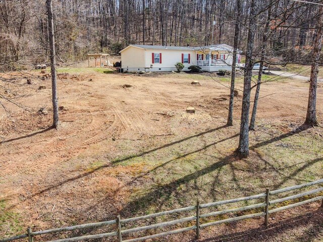 manufactured / mobile home featuring a view of trees, covered porch, and fence