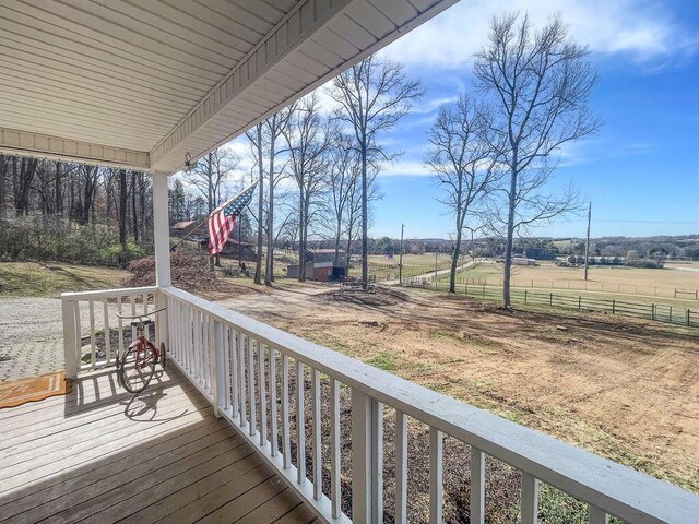 wooden terrace featuring a rural view, a porch, and fence