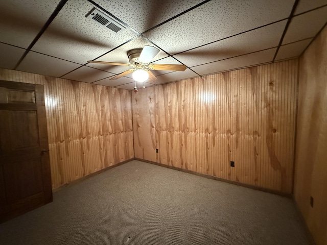 finished below grade area with wood walls, a drop ceiling, carpet flooring, and visible vents