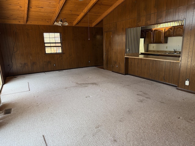 unfurnished living room featuring vaulted ceiling with beams, light carpet, a sink, wooden walls, and wooden ceiling