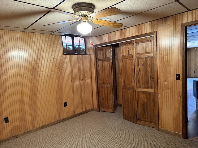 below grade area featuring light carpet, ceiling fan, baseboards, and wooden walls