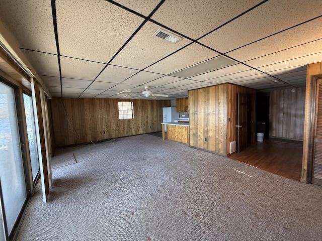 empty room with dark colored carpet, visible vents, wood walls, and a paneled ceiling