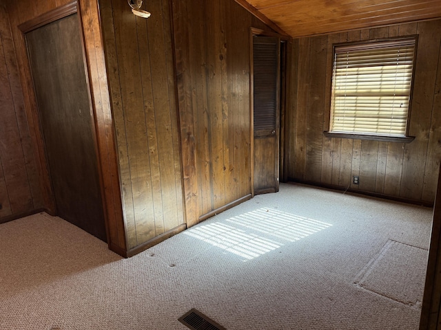 unfurnished room with wooden walls, vaulted ceiling, and light colored carpet