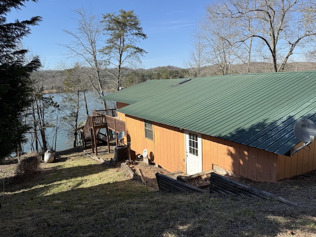 view of side of home featuring a yard, cooling unit, metal roof, and stairs