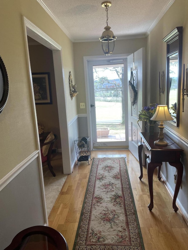 doorway with light wood-style floors, ornamental molding, a textured ceiling, and a wainscoted wall