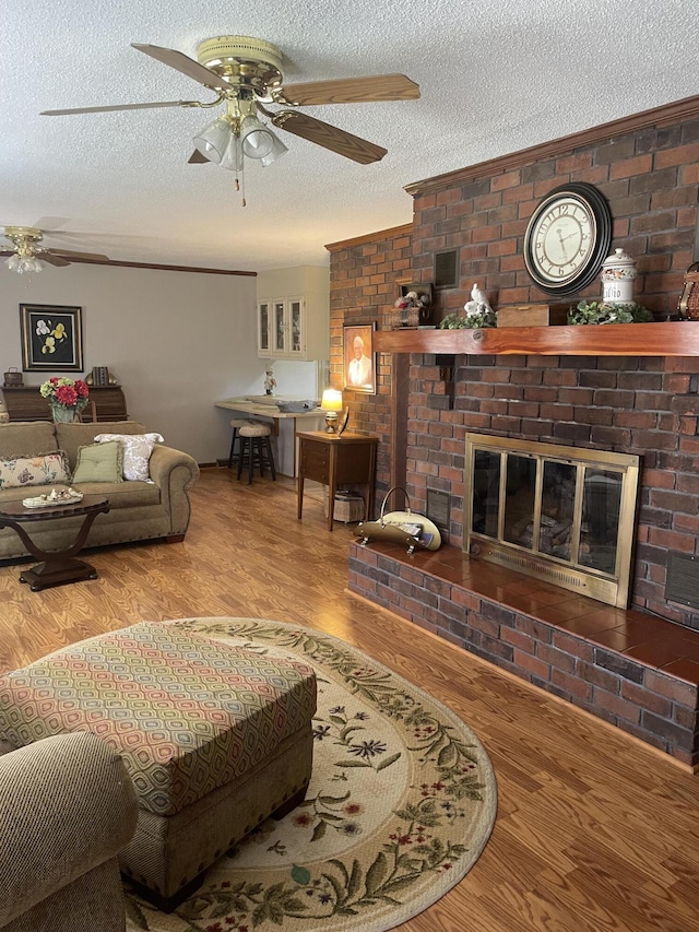 living room featuring a textured ceiling, a fireplace, wood finished floors, and a ceiling fan