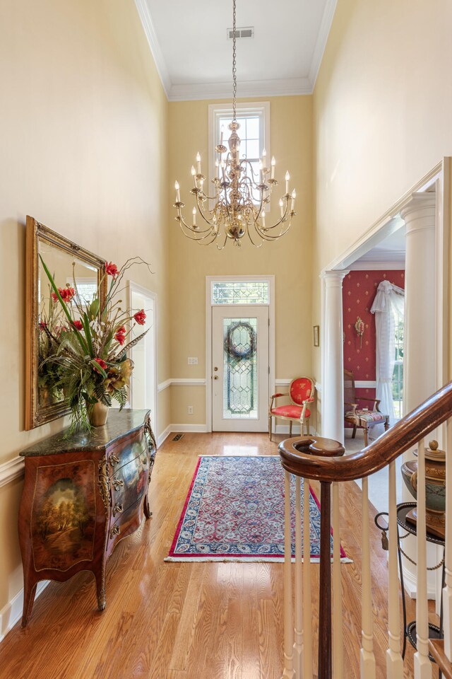 entryway featuring light wood-type flooring, decorative columns, ornamental molding, and a notable chandelier