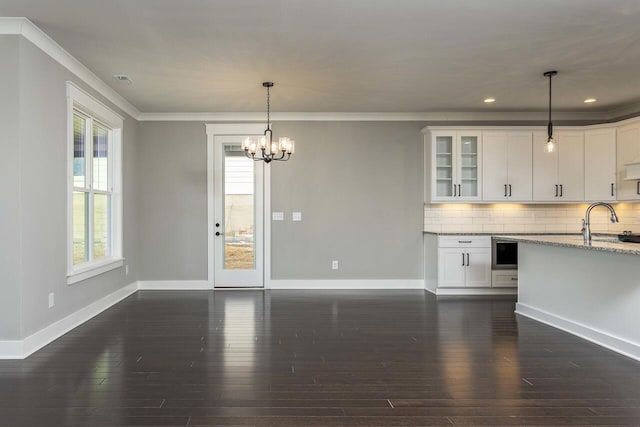 kitchen featuring light stone countertops, pendant lighting, white cabinets, backsplash, and a chandelier