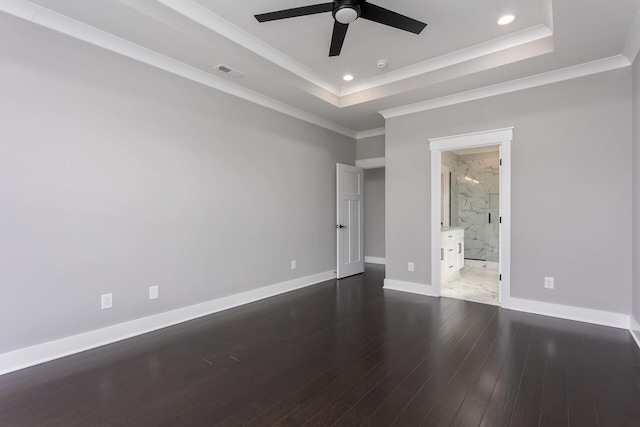 unfurnished bedroom featuring ceiling fan, ensuite bathroom, dark hardwood / wood-style floors, and a tray ceiling