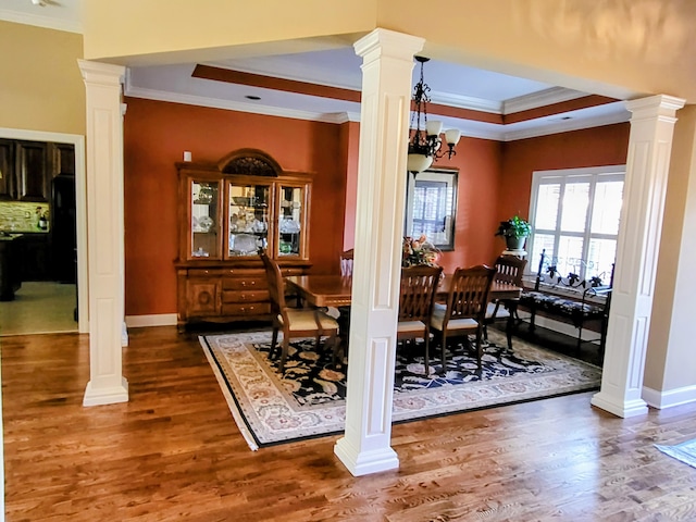 dining area with dark wood-type flooring, ornamental molding, a raised ceiling, and ornate columns