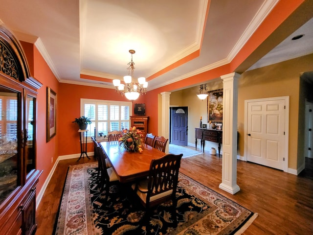 dining space featuring decorative columns, ornamental molding, a raised ceiling, dark wood-type flooring, and an inviting chandelier