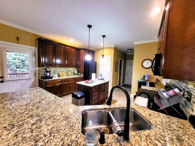 kitchen with sink, hanging light fixtures, ornamental molding, light stone countertops, and backsplash