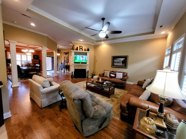 living room featuring crown molding, ceiling fan with notable chandelier, decorative columns, and a raised ceiling