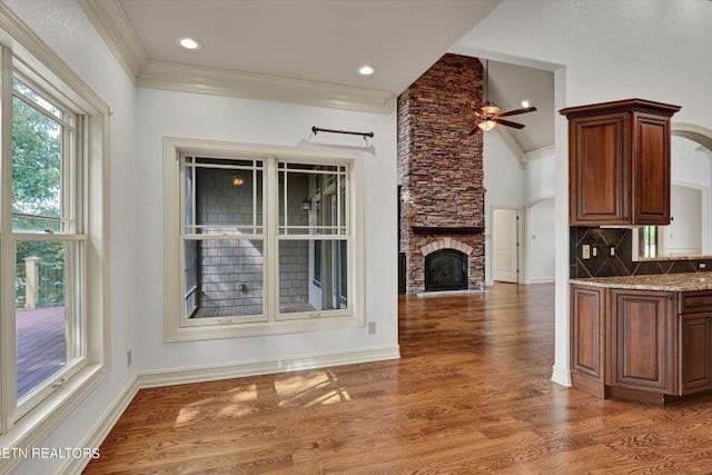 kitchen featuring a stone fireplace, crown molding, dark hardwood / wood-style floors, ceiling fan, and backsplash