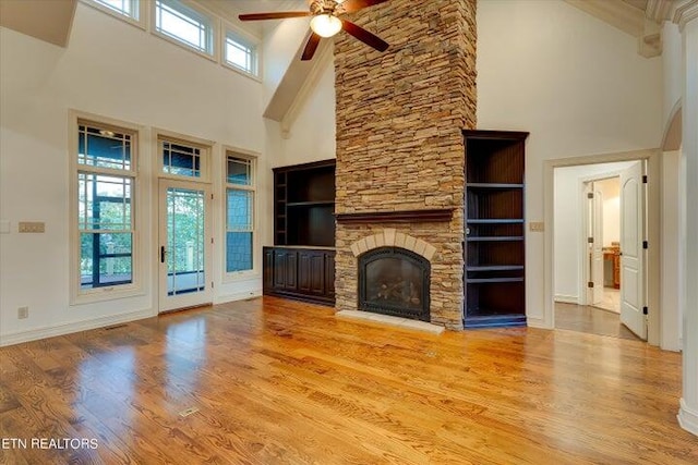 unfurnished living room with hardwood / wood-style flooring, ceiling fan, a stone fireplace, and a towering ceiling