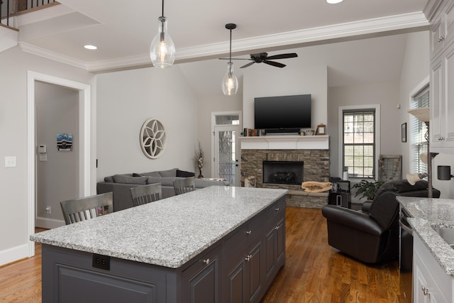 kitchen featuring dark wood-type flooring, white cabinets, a stone fireplace, ceiling fan, and light stone countertops