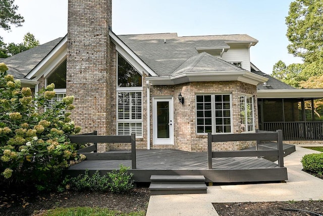 back of house with a shingled roof, a sunroom, and a wooden deck