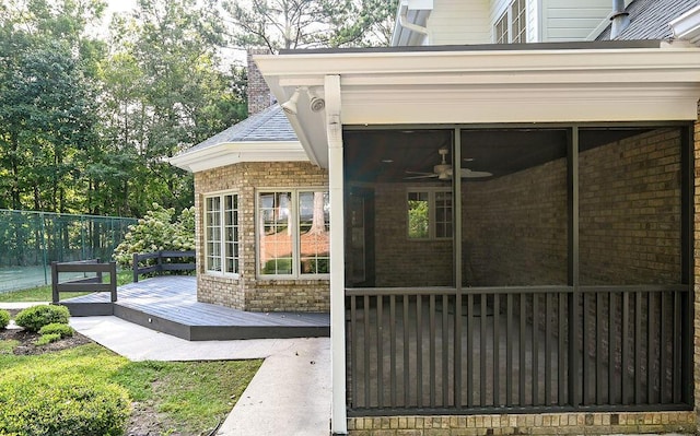 view of exterior entry featuring brick siding, a chimney, ceiling fan, fence, and a wooden deck