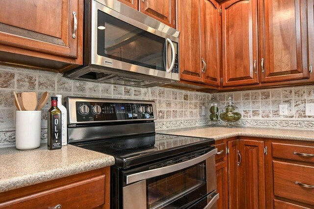 kitchen with stainless steel appliances, backsplash, light countertops, and brown cabinetry