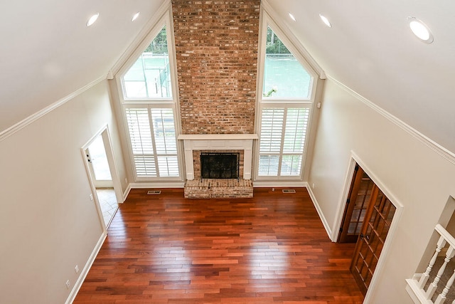 unfurnished living room with a towering ceiling, a fireplace, ornamental molding, and dark hardwood / wood-style floors