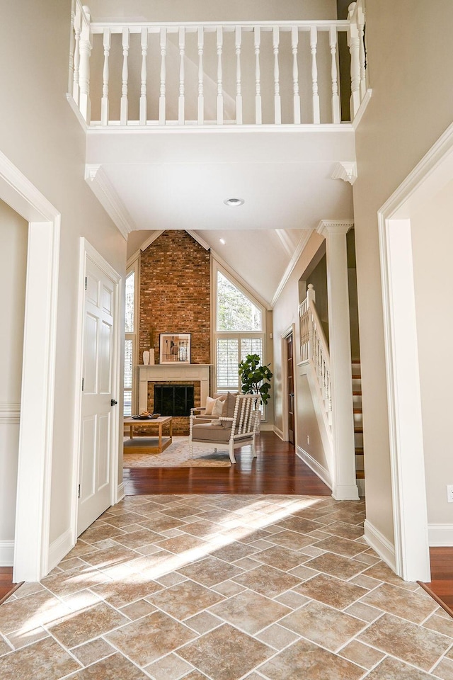 entryway with baseboards, stairs, stone tile flooring, a brick fireplace, and high vaulted ceiling